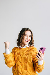 A joyful young woman, student or professional, celebrating success with a smartphone in hand....