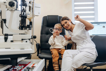 Sitting with doctor. Little boy is having check up in the ophthalmologist cabinet