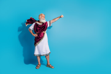 Full length photo of attractive old man raise fist flying dressed greek god emperor actor costume isolated on blue color background