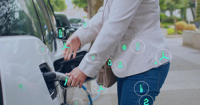 Image of eco icons over caucasian woman charging electric car