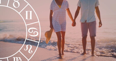 Image of horoscope over biracial couple holding hands at beach