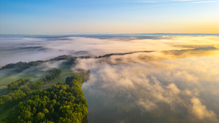 Obraz premium A calm morning blankets Rozmberk Pond in Trebon, Czechia, with mist gently rising from the water. Soft hues of sunrise reflect on the serene landscape, creating a tranquil atmosphere.