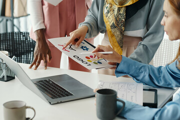 Group of professionals reviewing design concepts and notes around a laptop on a table. Papers and charts are seen, indicating a creative and collaborative discussion