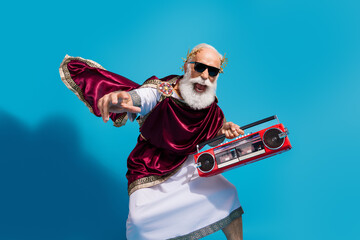 Photo of positive optimistic man wearing mantle clothes hold radio crazy dance isolated on blue color background