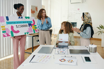 Diverse group of women celebrating startup pitch deck win in modern office setting with winner...