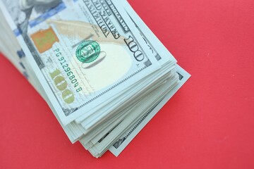 Big amount of hundred dollar bills in thick stack lies on bright red color paper background
