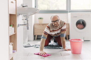 Frustrated man cleaning the wet floor in the bathroom