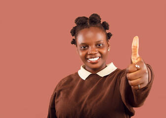 Young woman in a brown shirt making a thumbs-up sign against a coral background. Perfect for...