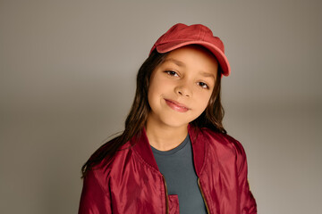 A cheerful girl wearing a cozy jacket and cap beams with excitement for Christmas cheer.