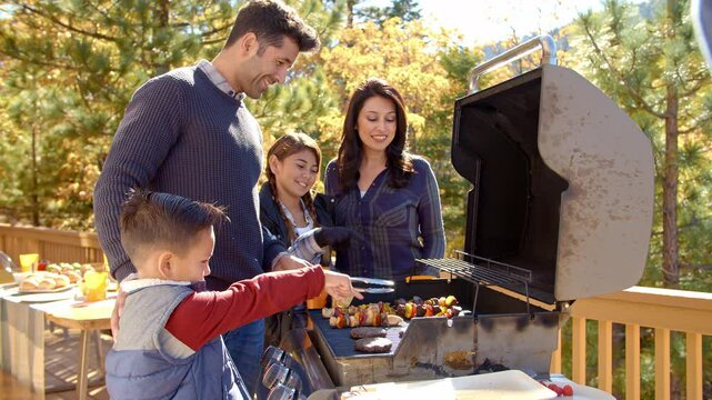 Handheld shot of family outdoor barbecue at home with father cooking food standing on wooden deck in  autumn garden - shot in slow motion