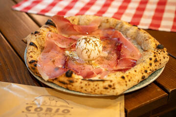 A close-up view of a pizza topped with burrata and thinly sliced prosciutto showcases its freshness and appeal.