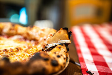 A slice of freshly baked pizza with gooey cheese, resting on a red-and-white checkered tablecloth.
