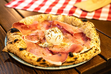 A delicious pizza topped with fresh prosciutto and creamy burrata, presented on a rustic plate.