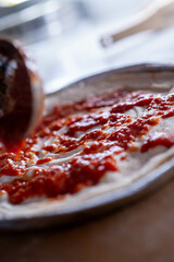 Fresh tomato sauce is evenly spread on a pizza base, capturing the start of a flavorful journey.