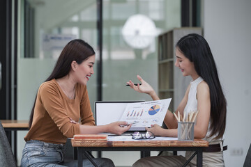 Two young Asian businesswomen discussed investment project work and planning strategy. Business people talk together on laptop computers at the office.