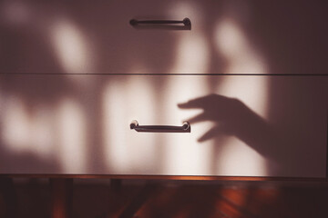 hands shadow trying to open a closed drawer. theft concept. fear. phobia. Cabinet drawer. forbidden...