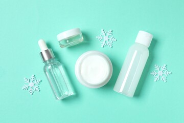 Winter skin care concept. Cosmetic products packaging design. Dropper bottle with serum, moisturizer cream jar and snowflakes on gray background. Flat lay, top view.