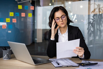 Businesswoman in office analyzing documents, discussing on smartphone, multitasking with laptop,...