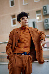 Young man in stylish brown outfit standing confidently against a modern urban backdrop