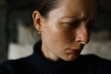 Sad woman 30-35 year old looking away and frowning close up in room at night. Sadness.