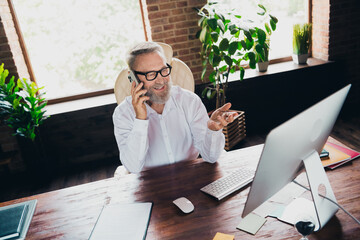 Photo of successful confident senior man entrepreneur banker speaking phone indoors workstation...