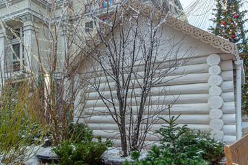 A white wooden house made of rounded logs and Christmas tree decorations on Christmas Eve. Festive...