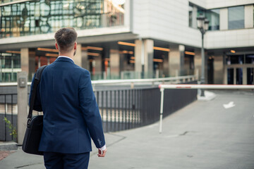 Fototapeta premium Businessman walking away in a modern cityscape with office buildings