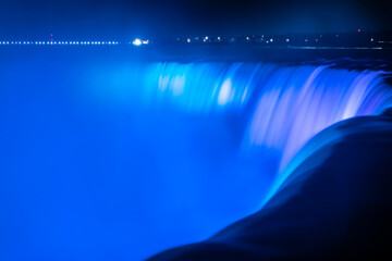 Blurred streams of Niagara Falls, illuminated in blue in the evening. Canada