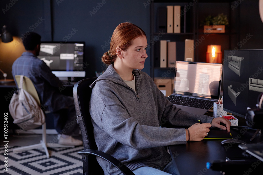 Poster portrait of woman sitting at desk in modern office working on computer with another person working i