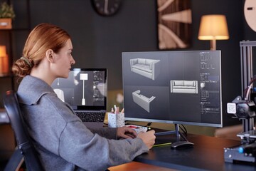 Woman sitting at desk, focusing on 3D modeling software displayed on her computer screen. Office...