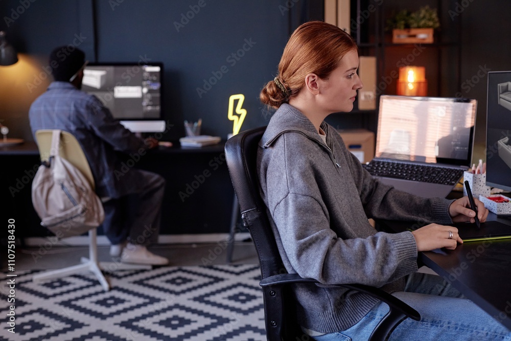 Poster woman sitting at desk with digital tools working on project while colleague at separate desk in mode