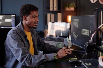 Man working at desk using computer to design 3D models of furniture Lighting from screens and multiple monitors enhancing workspace ambiance
