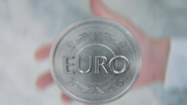 A hand flips a coin marked Dollar and Euro, spinning toward the camera in slow motion