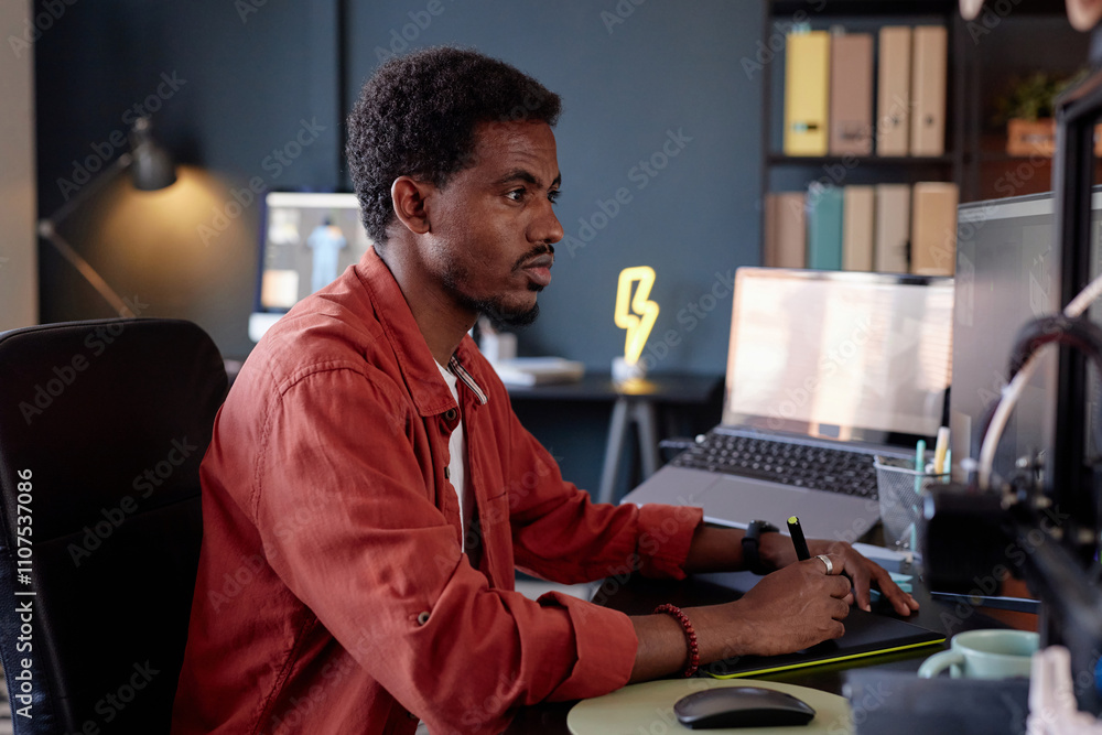 Poster Man working late in modern office, concentrating on task. Sitting at desk with computer, bookshelves in background, surrounded by office supplies