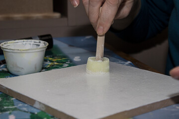 Creative workshop activity featuring hands crafting with paint on a canvas in a cozy setting