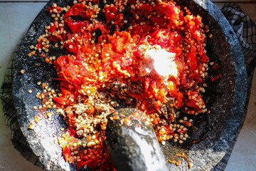 Sambal preparation in a stone mortar. Red chilies, salt, and other spices are being ground to...