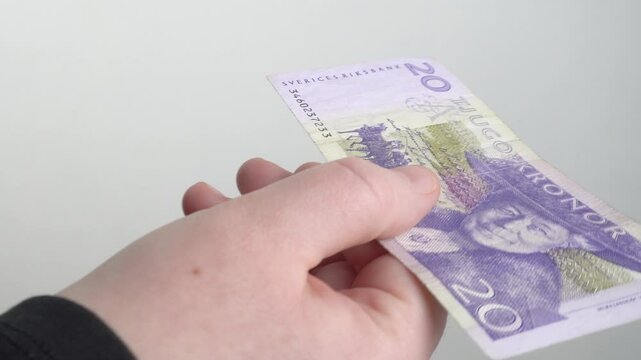 Women's hands with an old-style 20 Swedish kronor bill. 
hands are holding and examining an old banknote with a face value of 20 Swedish kronor. 