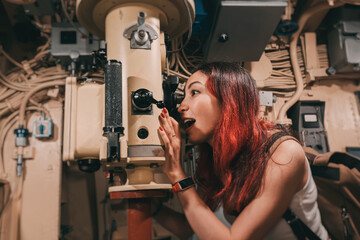 Young woman exploring submarine interior using periscope, experiencing naval history