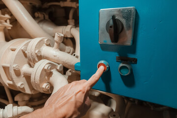 Hand activating emergency stop button on heavy machinery control panel in factory
