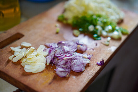 Close-up of sliced garlic, red onions, and spring onions neatly arranged on a rustic wooden cutting board, ready for cooking. Chopped Garlic, Red Onions, and Spring Onions on Wooden Cutting Board. - Powered by Adobe