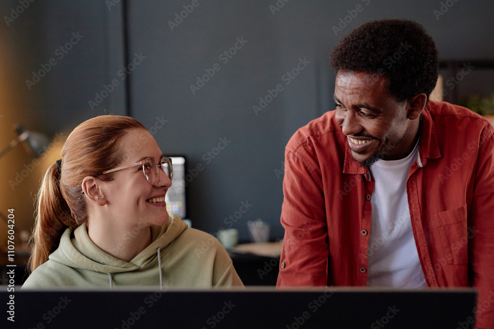 Poster smiling colleagues engaged in discussion in a modern office setting. person with glasses wearing hoo