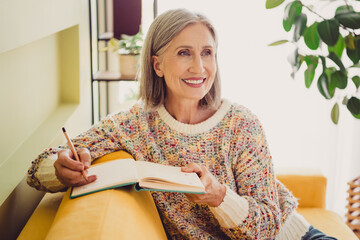 Elderly woman enjoying a peaceful afternoon writing in her journal while sitting in a comfortable...