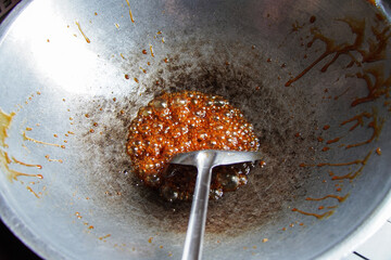 Close-up view of caramel bubbling in a wok during the cooking process. The wok shows signs of...