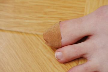 adhesive plaster on the big toe with nail injury. The background is a wooden surface.