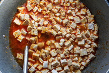 Close-up view of tempeh cubes simmering in a rich, spicy sauce inside a wok. Tempeh in Spicy Sauce.