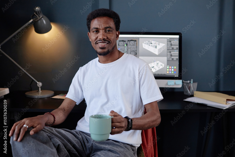 Poster portrait of cheerful man looking at camera while holding coffee cup, with computer displaying design
