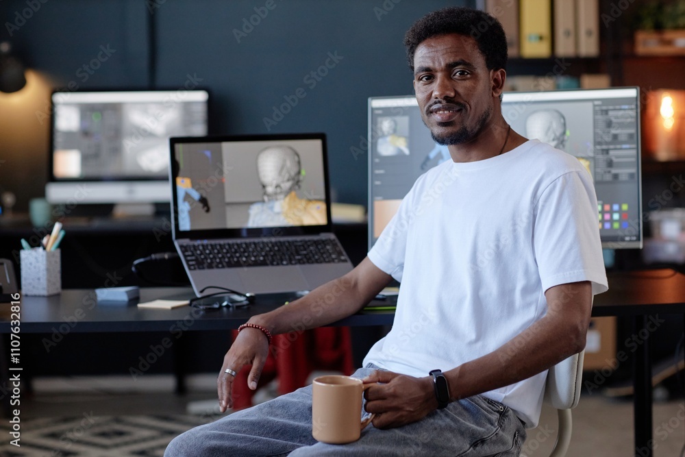 Poster portrait of african american man holding coffee cup while sitting at desk with computers in modern o