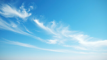 Obraz premium A few white clouds float serenely in a clear bright blue sky with only a slight hint of wispy strands at the horizon, empty canvas, natural beauty