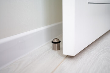 Door stopper on a light wooden floor next to a white door and wall skirting, providing protection...