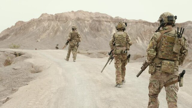 Soldiers in camouflage uniforms aiming with their rifles ready to fire during military operation in the desert